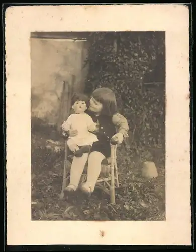 Fotografie glückliches Mädchen mit Puppe auf Korbsessel sitzend