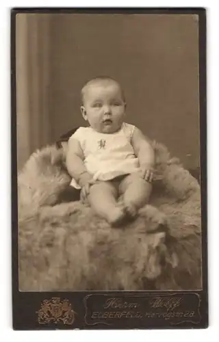 Fotografie Herm. Wolff, Elberfeld, Herzogstrasse 28, Baby auf einem Fell sitzend