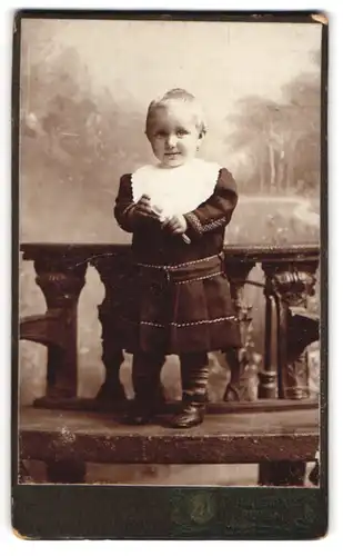 Fotografie A. Jandorf & Co., Berlin, Bellealliancestrasse 1 /2, Kleinkind auf einer Bank stehend