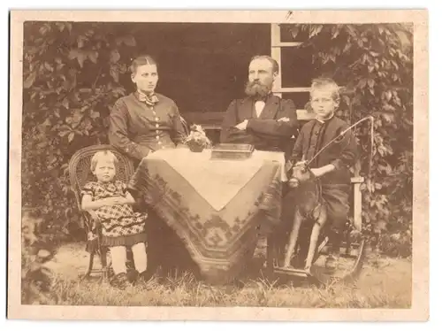 Fotografie unbekannter Fotograf und Ort, Eltern mit ihrem Kindern samt Schaukelpferd im Garten