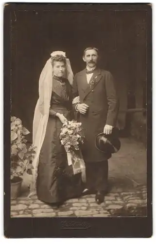 Fotografie E. Schädler, Ort unbekannt, Ehepaar im schwarzen Brautkleid und im Anzug mit Zylinder