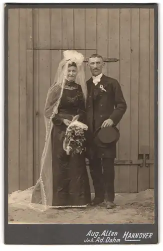 Fotografie Aug. Alten, Hannover, niedersächsisches Brautpaar im schwazen Brautkleid in im Anzug vor der Scheune