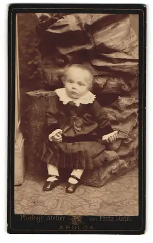 Fotografie Fritz Rath, Apolda, niedliches kleines Kind im Kleid vor einer Felsen Studiokulisse