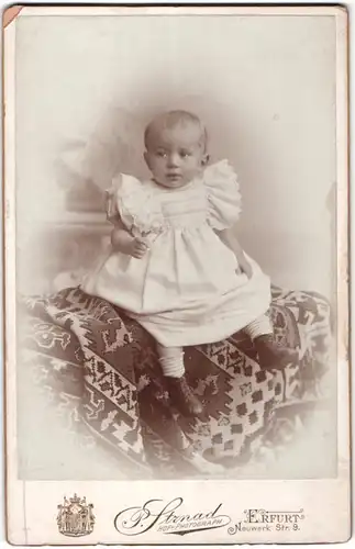 Fotografie P. Strnad, Erfurt, Portrait niedliches Kleinkind im weissen Kleid auf Decke sitzend