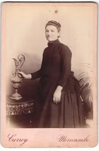 Fotografie W. Currey, Morecambe, Portrait bürgerliche Dame mit Kanne an Tisch gelehnt