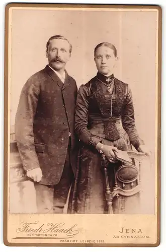 Fotografie Friedr. Haack, Jena, Portrait hübsch gekleidetes Paar mit Buch an Stuhl gelehnt