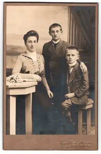 Fotografie Rud. Löbner, München, Portrait hübsche Dame in modischer Kleidung mit zwei Knaben am Tisch