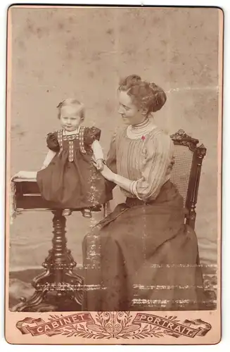 Fotografie Cabinet Portrait, unbekannter Ort, Portrait modisch gekleidete Dame und auf Tisch sitzendes kleines Mädchen