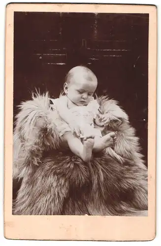 Fotografie unbekannter Fotograf und Ort, Portrait niedliches Kleinkind im weissen Hemd auf Fell sitzend