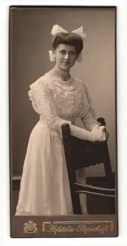 Fotografie Atelier Pieperhoff, Halle a / S., Portrait hübsche Dame im weissen Kleid an Stuhl gelehnt