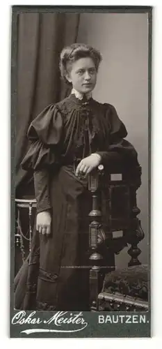 Fotografie Oskar Meister, Bautzen, Portrait hübsche Dame im schwarzen Kleid an Stuhl gelehnt