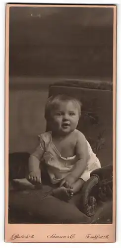 Fotografie Damson & Co., Frankfurt a / M., Portrait sitzendes Kleinkind im weissen Hemd mit nackigen Füssen