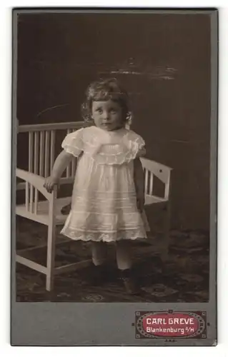 Fotografie Carl Greve, Blankenburg a / H., Portrait kleines Mädchen im weissen Kleid an Bank gelehnt
