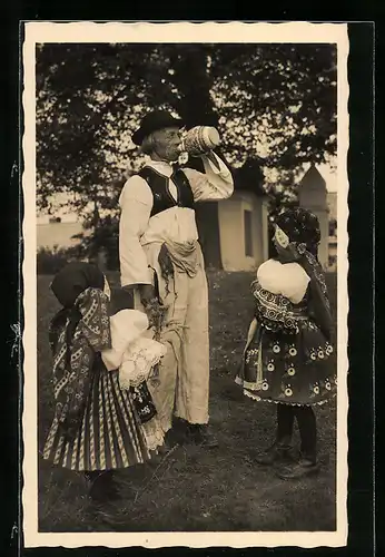 AK Aus einem Krug trinkender alter Mann und zwei kleine Mädchen in tschechischer Tracht