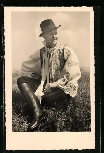 AK Kroje z Mor. slovácka, charmanter Mann in Tracht auf einer Wiese sitzend