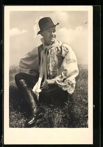 AK Kroje z Mor. slovácka, charmanter Mann in Tracht auf einer Wiese sitzend
