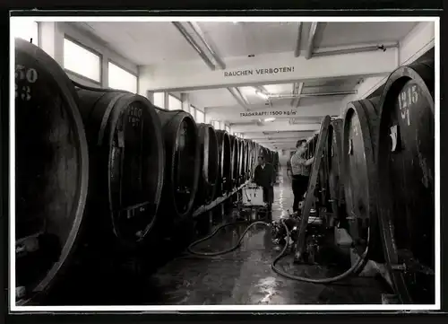 Fotografie Weinkellerei, Kellermeister zwischen Weinfässern bei der Arbeit