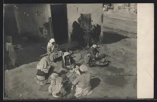 Foto-AK Auf der Strasse sitzende Familie vor einem Haus
