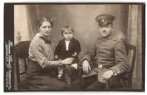 Fotografie Hermann Schmidt, Olbernhau, Freibergerstrasse 28, Unteroffizier in Feldgrau mit Frau und Kind