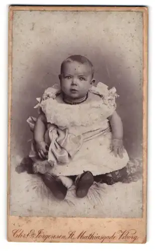 Fotografie Chr. & Jörgensen, Viborg, St. Mathiasgade, Niedliches Baby in weissem Kleid mit erschrockenem Blick