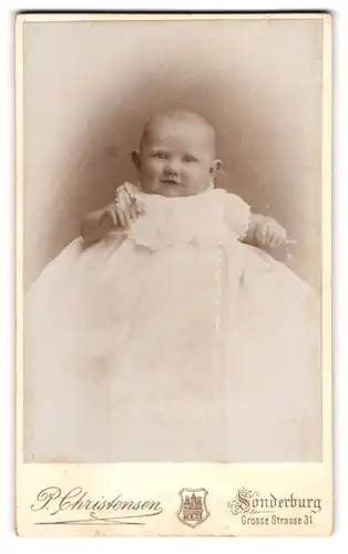 Fotografie P. Christensen, Sonderburg, Grosse Strasse 31, Niedliches Baby in weissem Kleid mit grossen Ohren und Lächeln