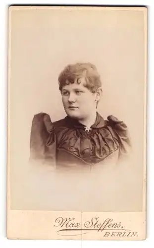 Fotografie Max Steffens, Berlin, Lothringer-Str. 54, Junge Dame in schwarzem Kleid mit Puffärmeln und silberner Brosche
