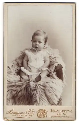 Fotografie Samson & Co, Frankfurt a. M., Zeil 46, Süsses Baby in weissem Kleid mit erstauntem Blick