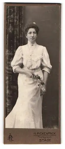 Fotografie H. Pickenpack, Stade, Gutaussehende brünette Dame im weissen Kleid und mit Blumen in der Hand