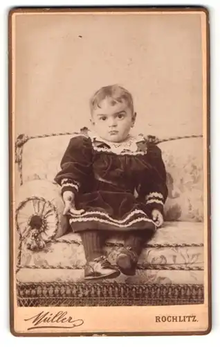 Fotografie Moritz Müller, Rochlitz, Portrait niedliches Kleinkind im Samtkleid auf Couch sitzend