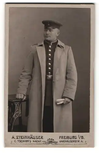 Fotografie A. Steinhäuser, Freiburg i / B., Portrait Soldat im Uniformmantel mit Schirmmütze und Handschuhen