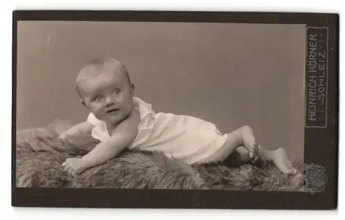 Fotografie Heinrich Körner, Schleiz, Portrait niedliches Kleinkind auf Fell liegend