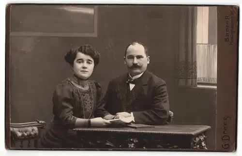 Fotografie G. Drees, Barmen R., Mann in Anzug mit Schnauzbart und Frau in bestickter Bluse sitzen an Tisch