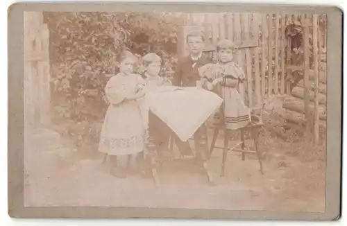 Fotografie unbekannter Fotograf und Ort, Junger Bursche sitzt mit seinen drei kleinen Geschwistern an einem Tisch