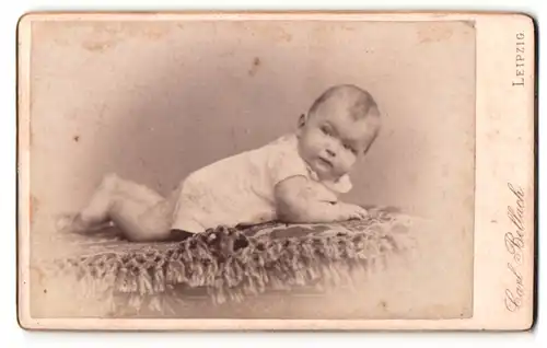 Fotografie Carl Bellach, Leipzig, Portrait süsses Baby liegt im weissen Hemdchen auf einem Fell