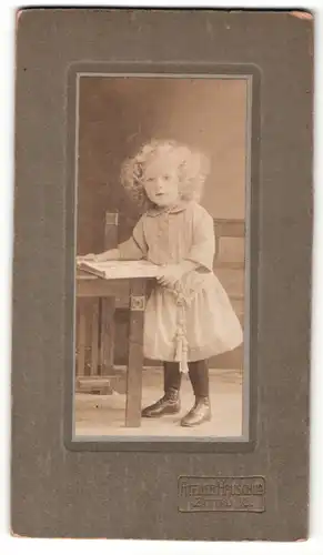 Fotografie Atelier Hauschild, Zittau i / S., Portrait kleines Mädchen mit Buch am Tisch stehend