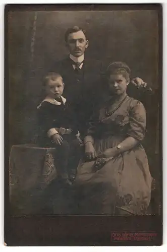 Fotografie Otto Hertel, Freiberg i / S., Portrait hübsch gekleidetes Paar mit einem Sohn am Tisch