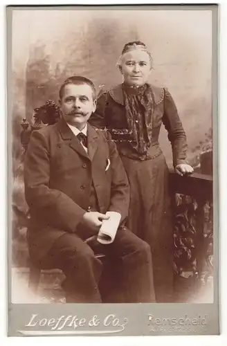 Fotografie Loeffke & Co., Remscheid, Portrait älteres Paar in hübscher Kleidung mit Zeitung