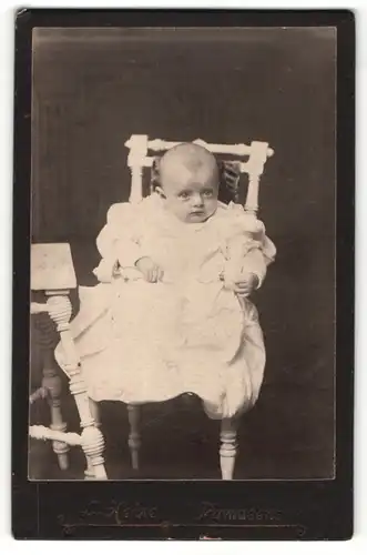 Fotografie L. Heine, Pirmasens, Portrait niedliches Baby im weissen Kleid im Kinderstuhl sitzend