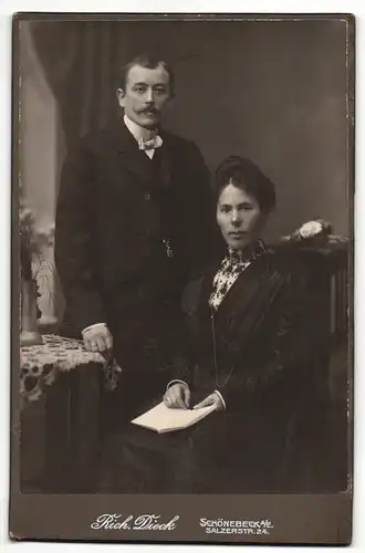 Fotografie Rich. Dieck, Schönebeck a / E., Portrait elegant gekleidetes Paar mit Buch am Tisch