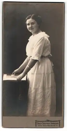 Fotografie Ernst Tremper, Hannover, Portrait weiss gekleidete Dame mit Zeitschrift an Tisch gelehnt