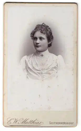 Fotografie E. W. Matthias, Seifhennersdorf, Portrait bezauberndes fräulein mit lockigem Haar im weissen Kleid