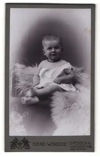 Fotografie Bruno Wendsche, Dresden-N, Portrait süsses Kleinkind im weissen Hemd auf Fell sitzend