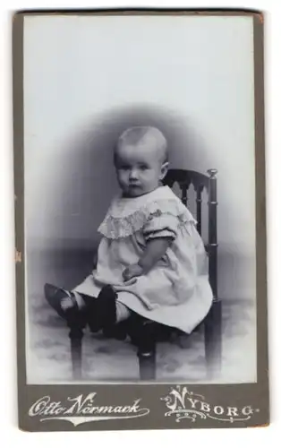 Fotografie Otto Nörmark, Nyborg, Kleinkind im Puffärmelkleidchen auf einem Stuhl