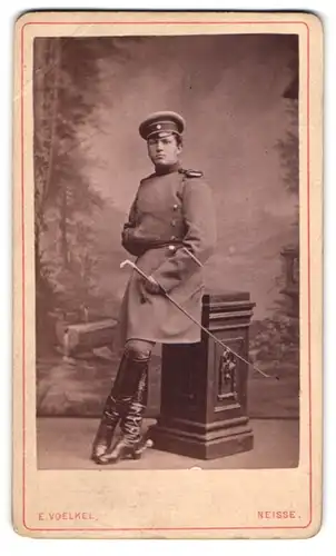 Fotografie E. Voelkel, Neisse, junger Soldat in Uniform mit Epauletten und Flanierstock, Uniformmantel