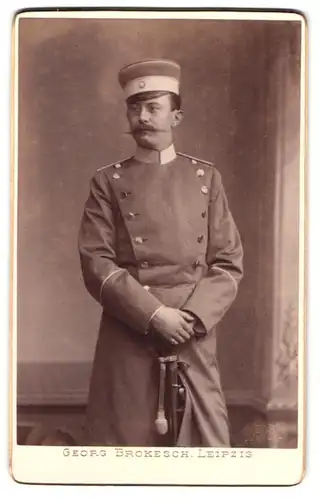 Fotografie Georg Brokesch, Leipzig, Soldat in Uniform Mantel mit Säbel und Mütze