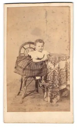 Fotografie unbekannter Fotograf und Ort, Kind in Bluse und Rock sitzt am Tisch