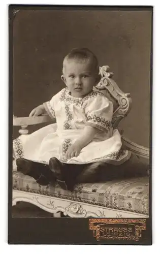 Fotografie Strauss, Leipzig, Windmühlenstr. 8, Niedliches Baby in weissem Kleid mit leicht entsetztem Blick