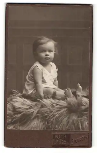Fotografie Rich. Vogel, Glauchau i. S., Portrait süsses kleines Mädchen im weissen Kleidchen auf Fell sitzend