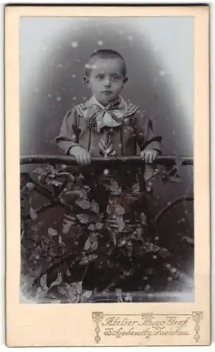 Fotografie Hugo Graf, Zwickau i. S., Portrait frecher Bube mit kurzem Haar am Geländer stehend