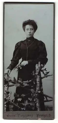 Fotografie Enst Freygang, Penig i. S., Portrait schwarz gekleidete Dame mit Blumen an Zaun gelehnt